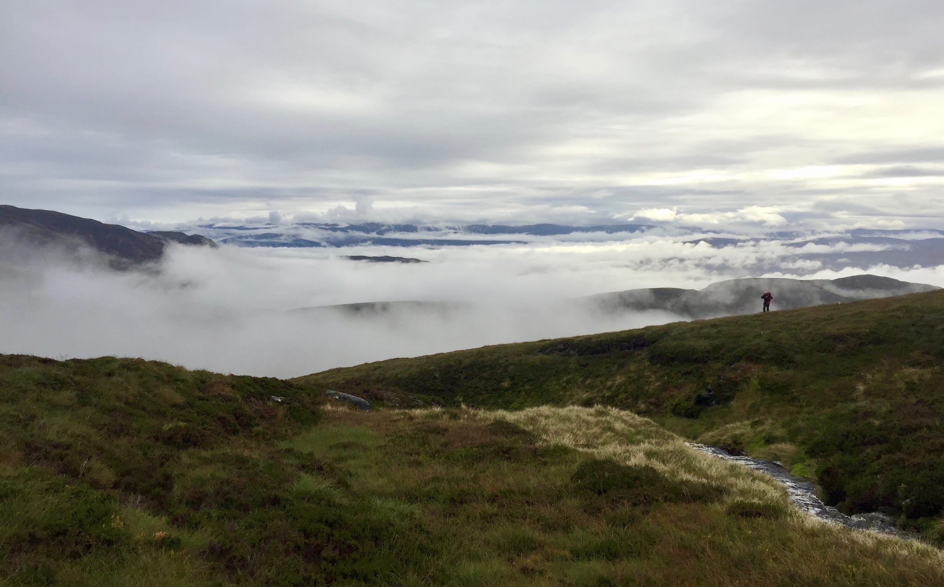 CLOUDED HORIZONS: A lone figure stands out against a backdrop of static white cloud during the ascent of A' Chailleach